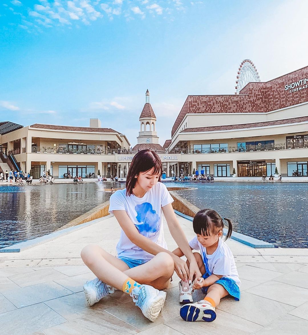 A woman and child sit by a fountain in front of a shopping mall