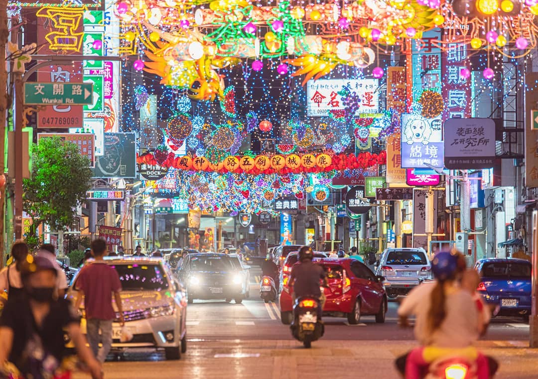 Bustling city street at night with colorful neon signs and festive lanterns overhead