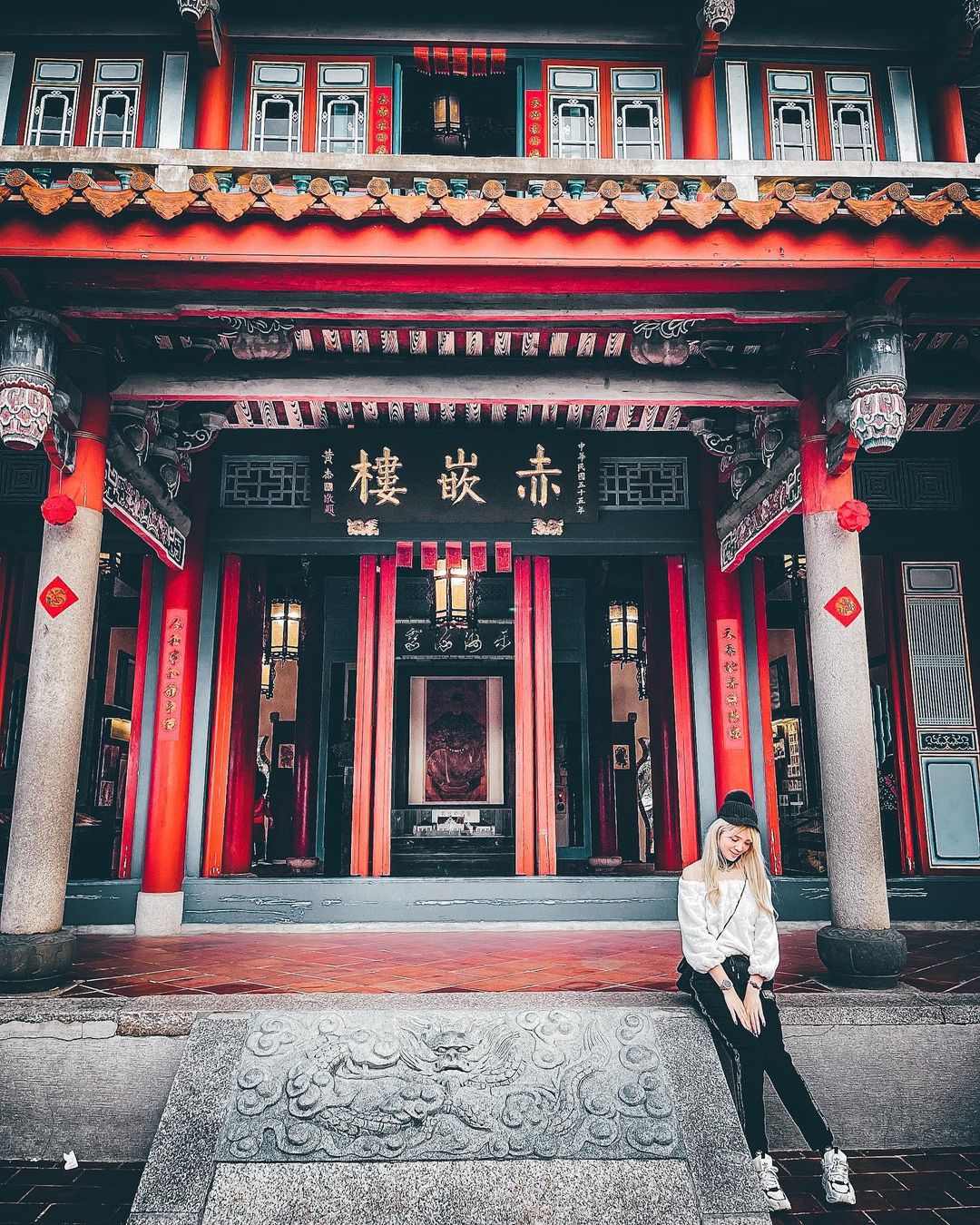 A woman sits in front of a traditional Chinese building