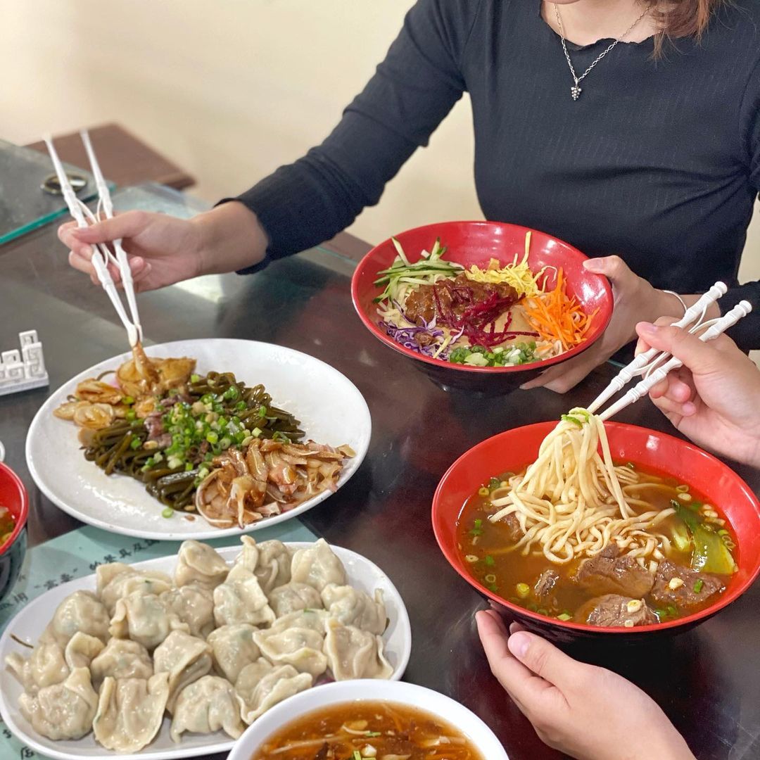 People sharing a meal of Chinese dumplings and beef noodle soup