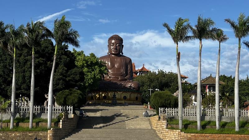 A large bronze Buddha statue sits serenely amidst lush greenery