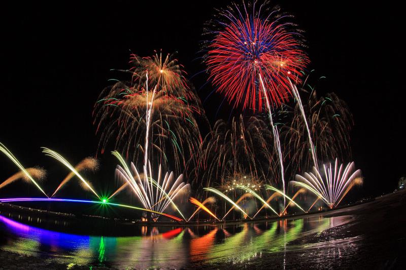 A vibrant fireworks display illuminates the night sky over water