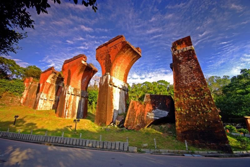 Remains of red brick bridge pillars stand amid lush greenery under a blue sky