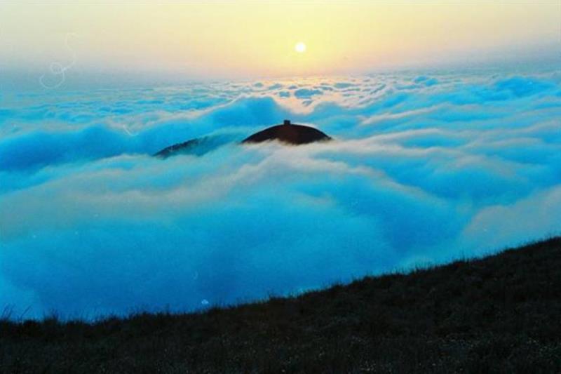 Sunrise above a cloud-covered landscape, with a mountain