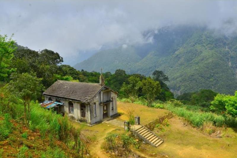 A small, rustic cottage sits on a grassy hillside