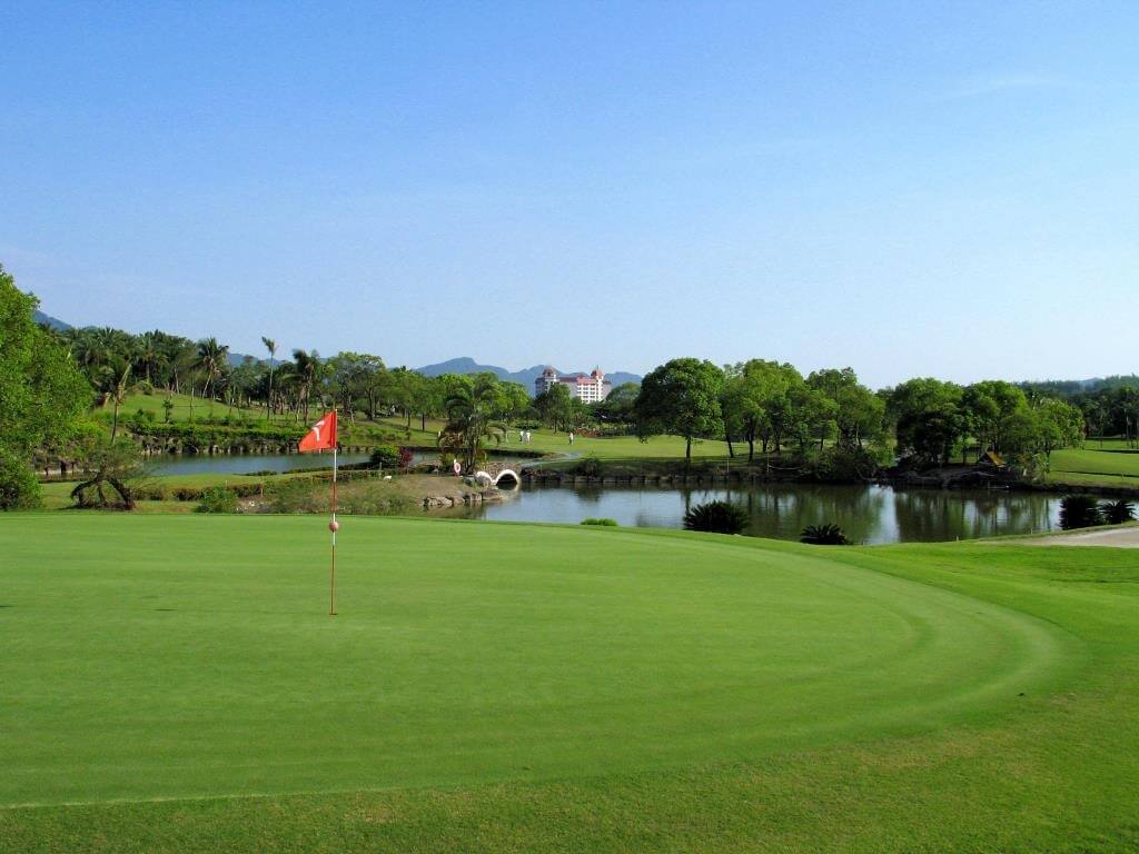 A sunlit golf course putting green with a red flag