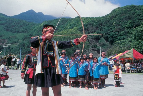 indigenous archer in traditional attire demonstrating a recurve bow