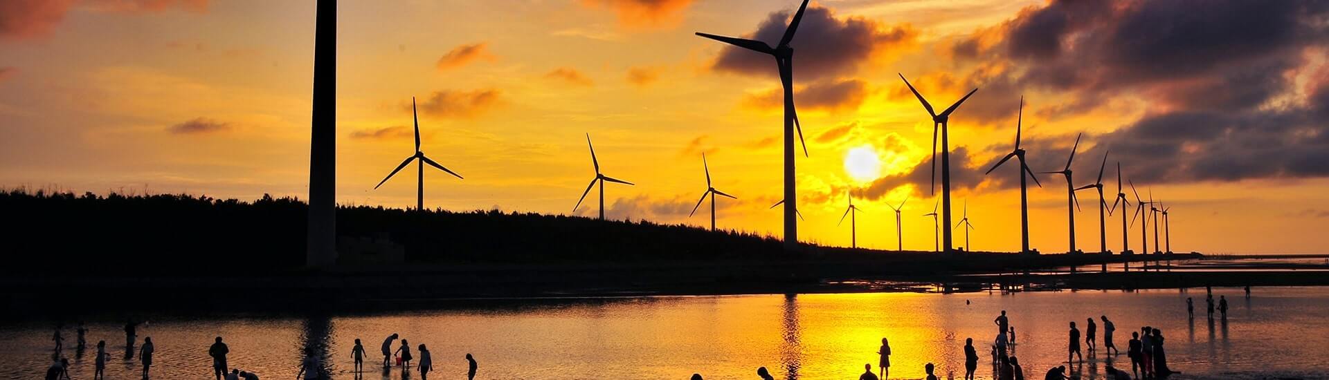 Silhouetted windmills along the coastline at Gaomei Wetlands during a warm sunset in Taichung.